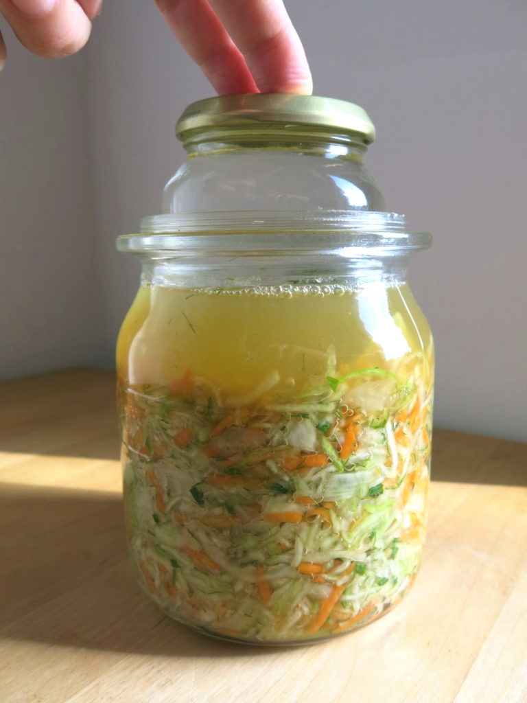 Einmachglas mit selbst angesetztem Sauerkraut, Hand drückt auf das Gewicht